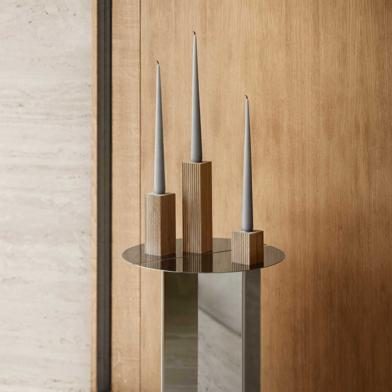 blomus DREVA oak taper candle holders on stainless steel table against a wood wall