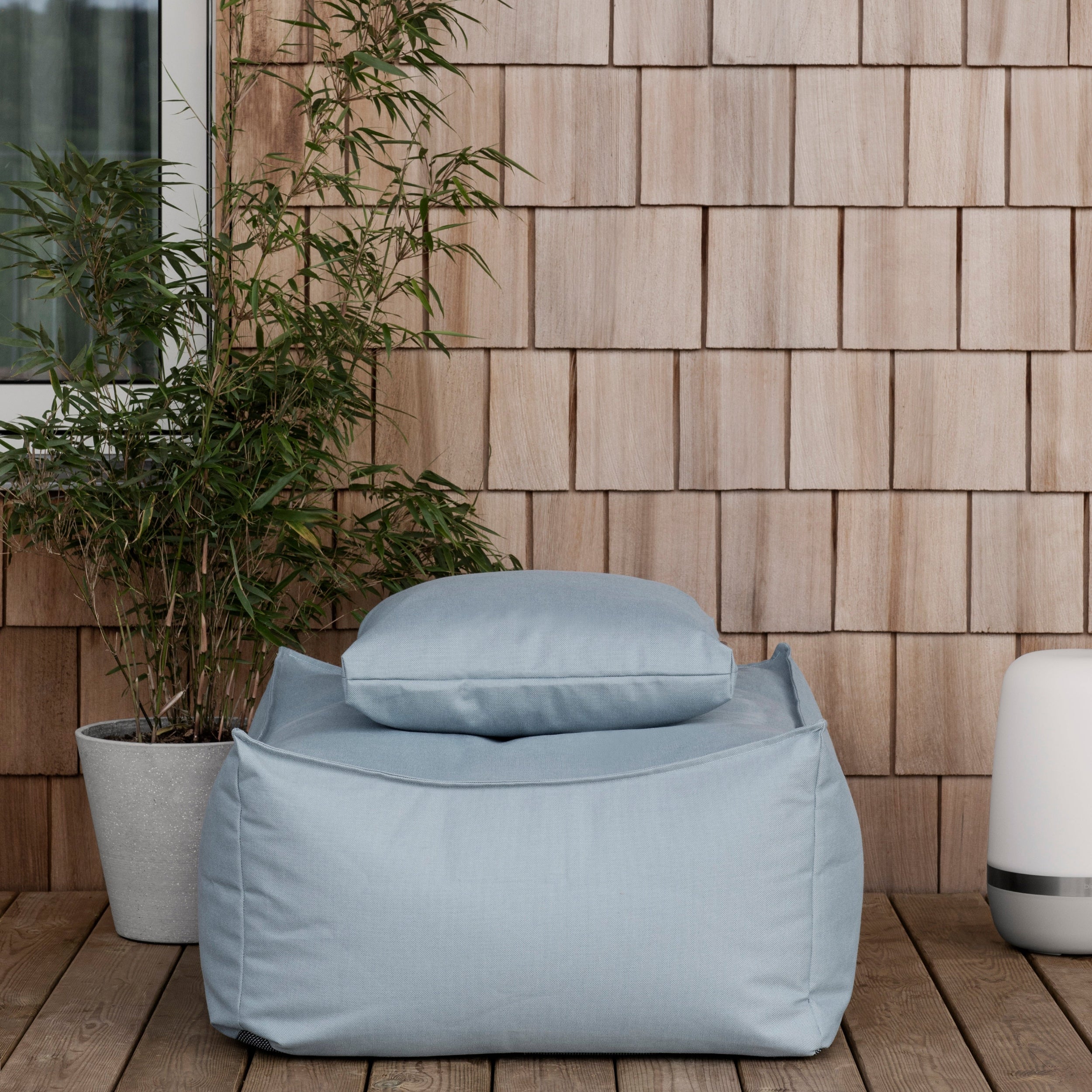 Light blue bean bag chair on a wooden deck with a wooden wall and plant in the background