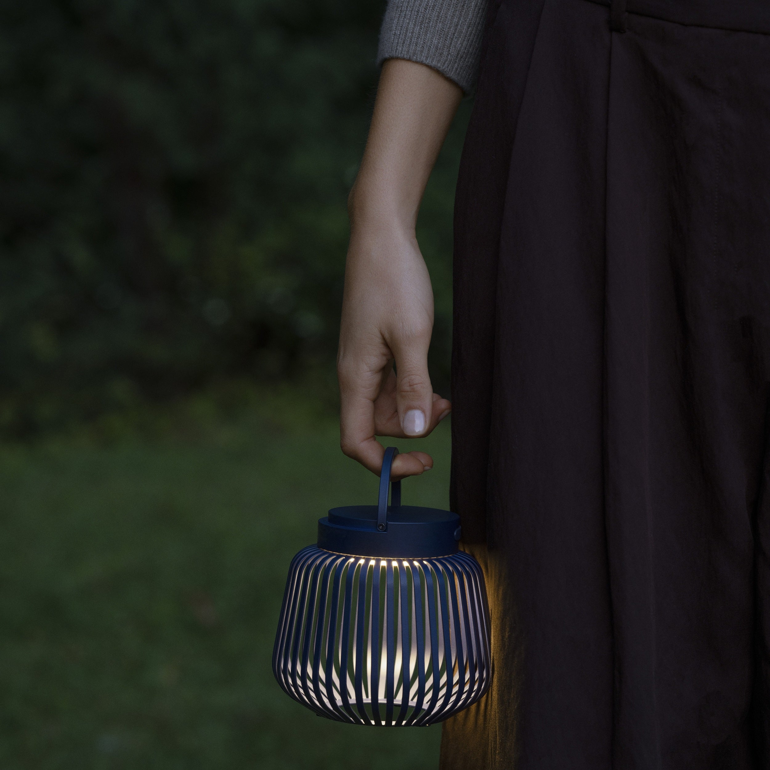 Black XS Lito Lantern being held by a woman's hand with grass in the background.