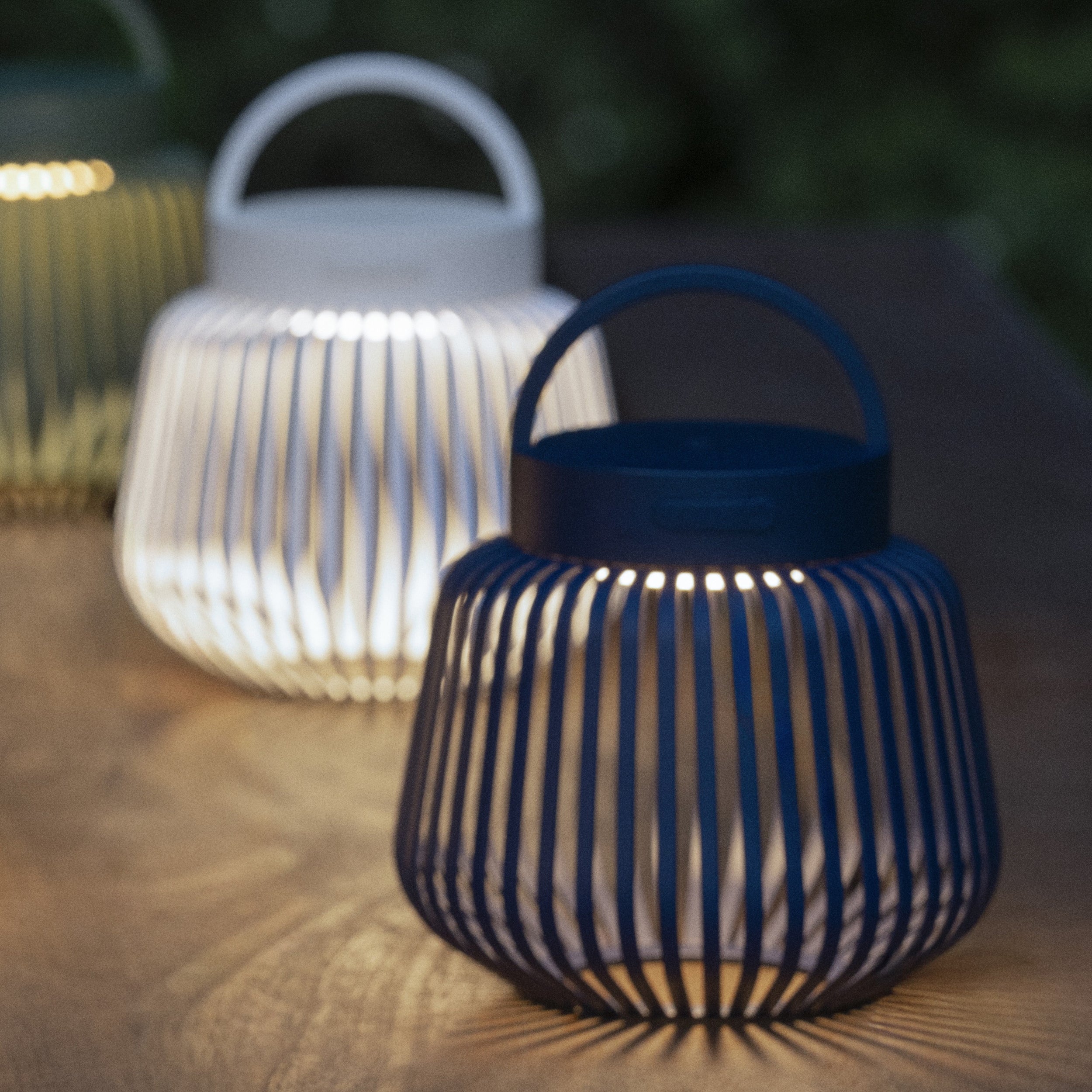 Two XS Lito lanterns, one black and one white, on a wooden surface with a blurred background.