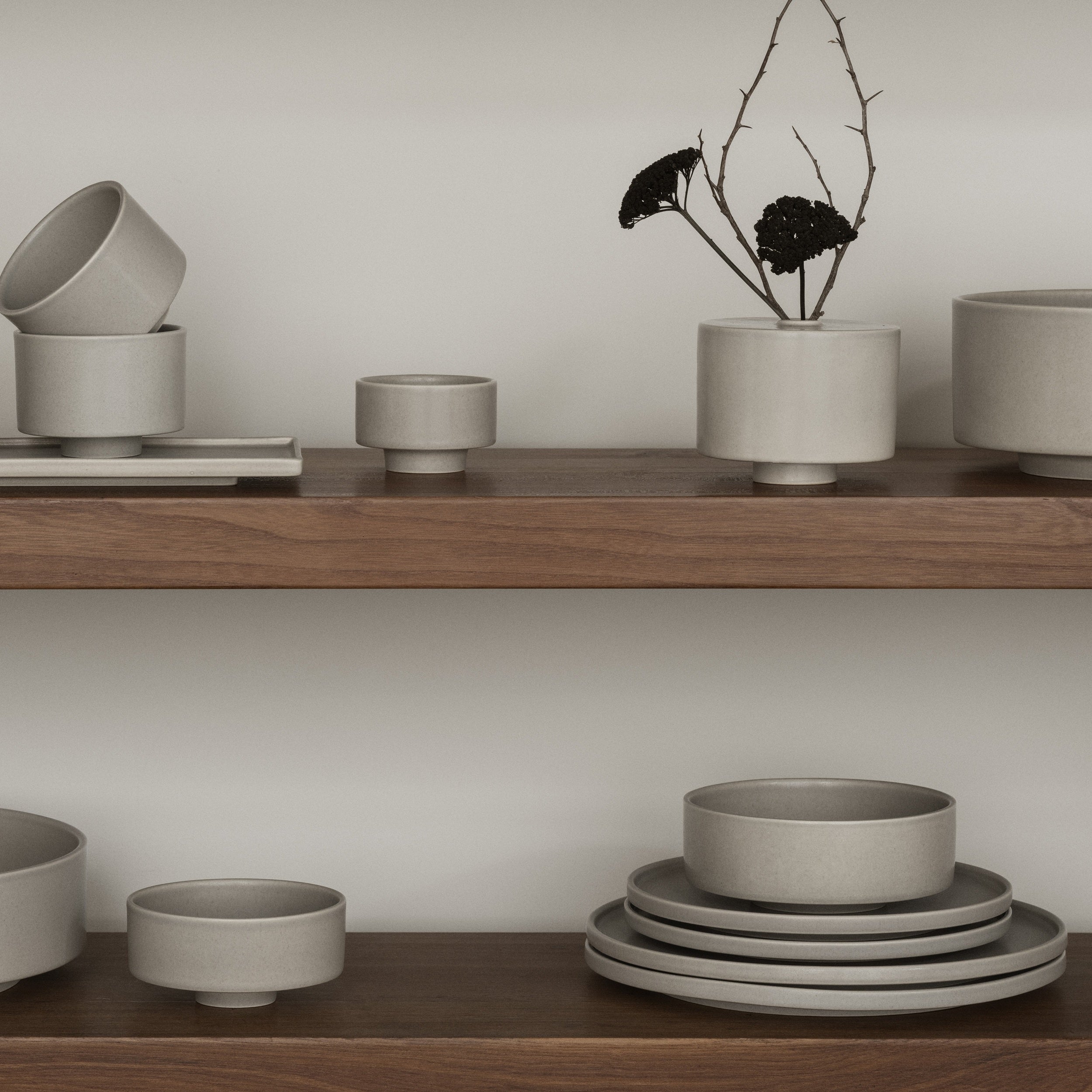 Set of gray ceramic bowls and planters on wooden shelves against a neutral wall.
