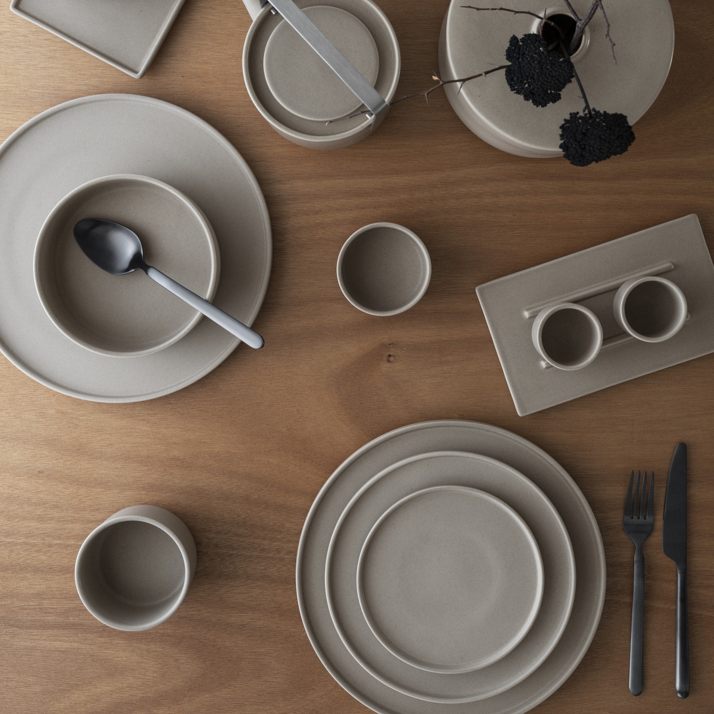 Set of gray ceramic dinnerware on a wooden table with cutlery.
