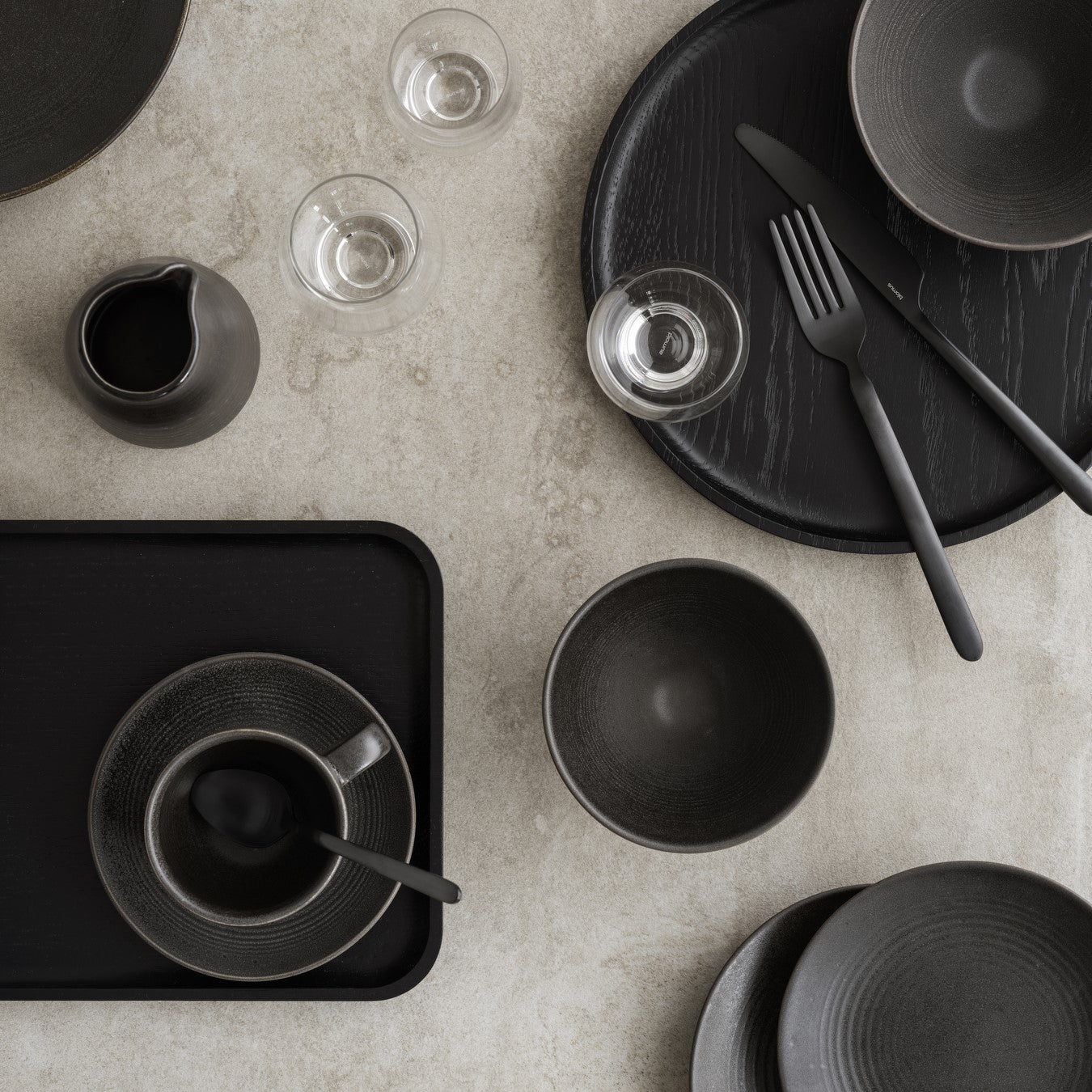 elegant dishware and black wood serving trays on natural stone surface