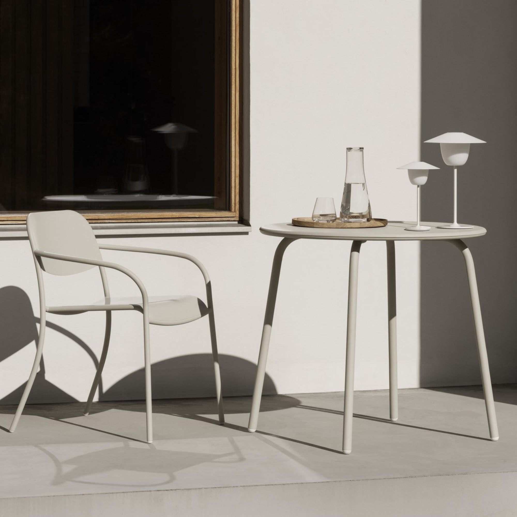 Outdoor patio with modern stackable  metal chair and table in cream color with water glass and lamps on table