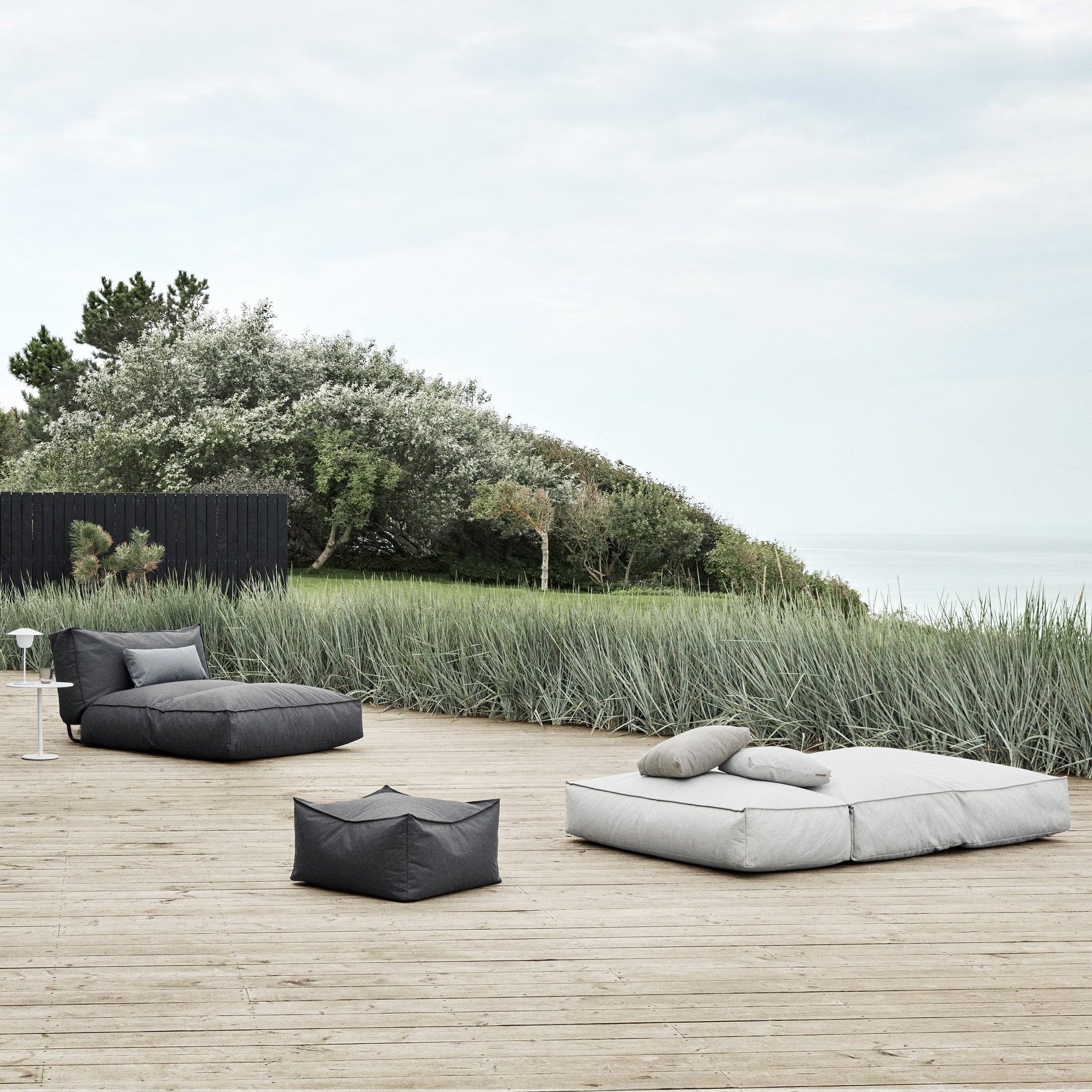 Large wooden deck with oversized outdoor loungers near swaying grasses
