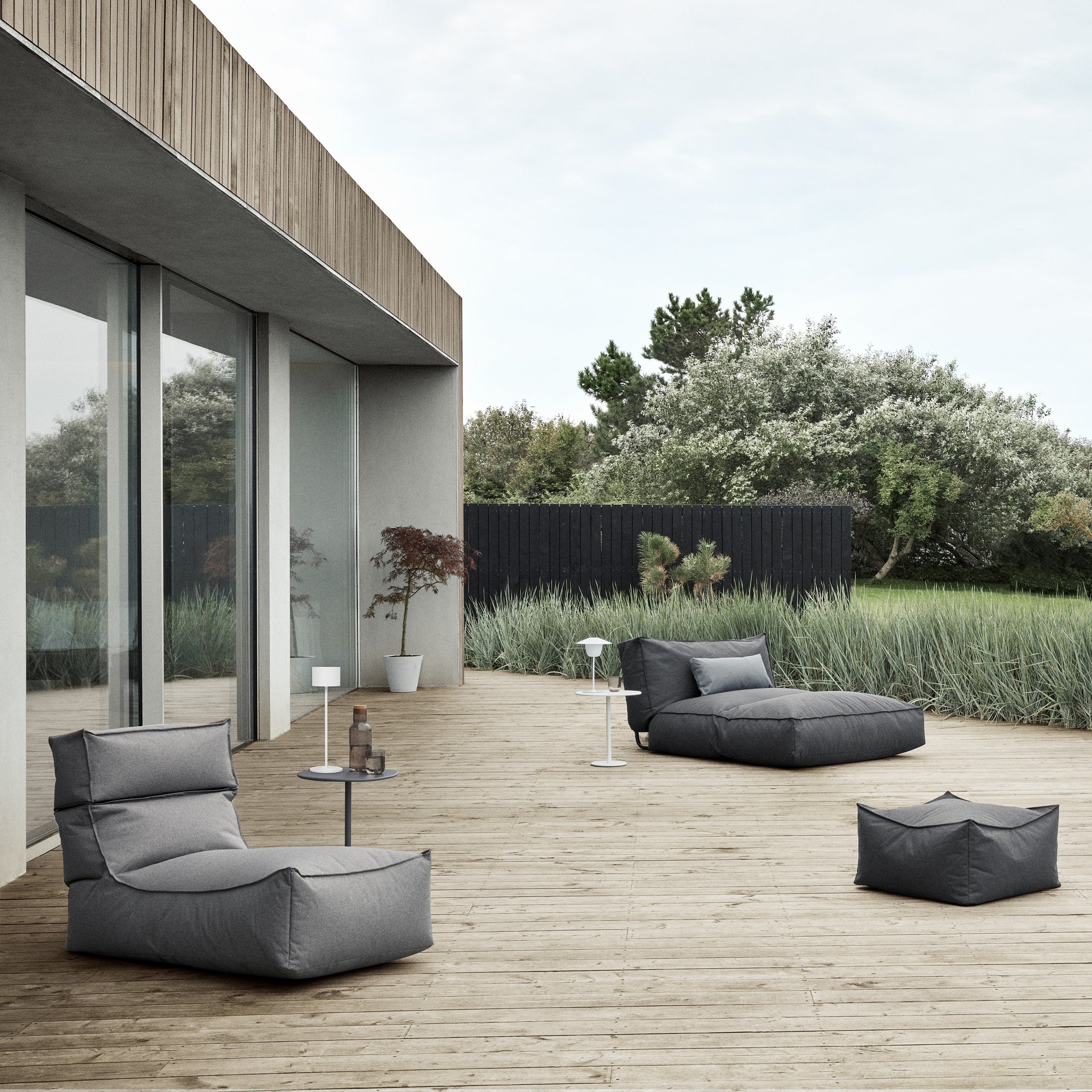 Wooden patio with comfy outdoor loungers in a modern backyard setting with tall grass