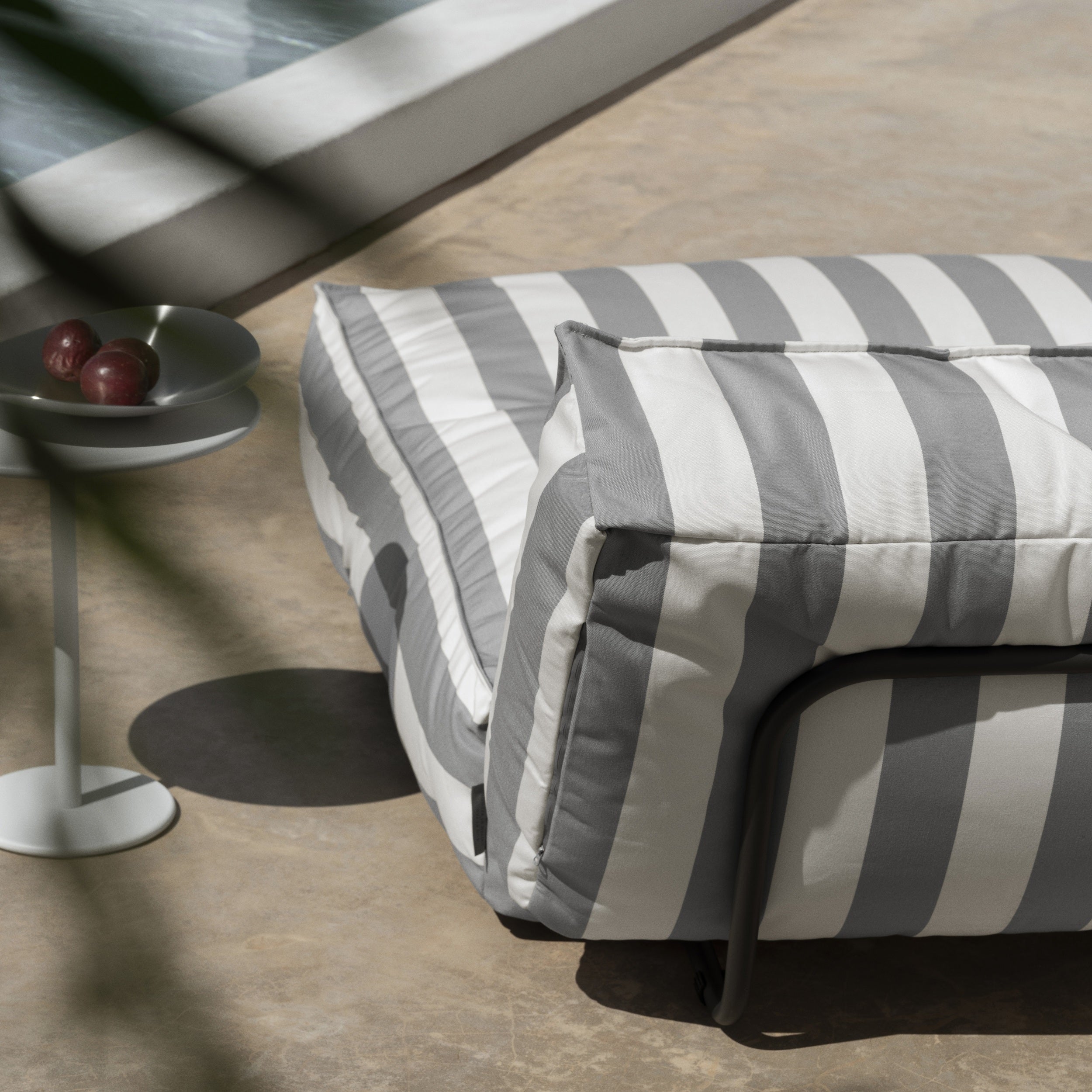 Gray and white striped ottoman on a wooden floor with a side table in the background.