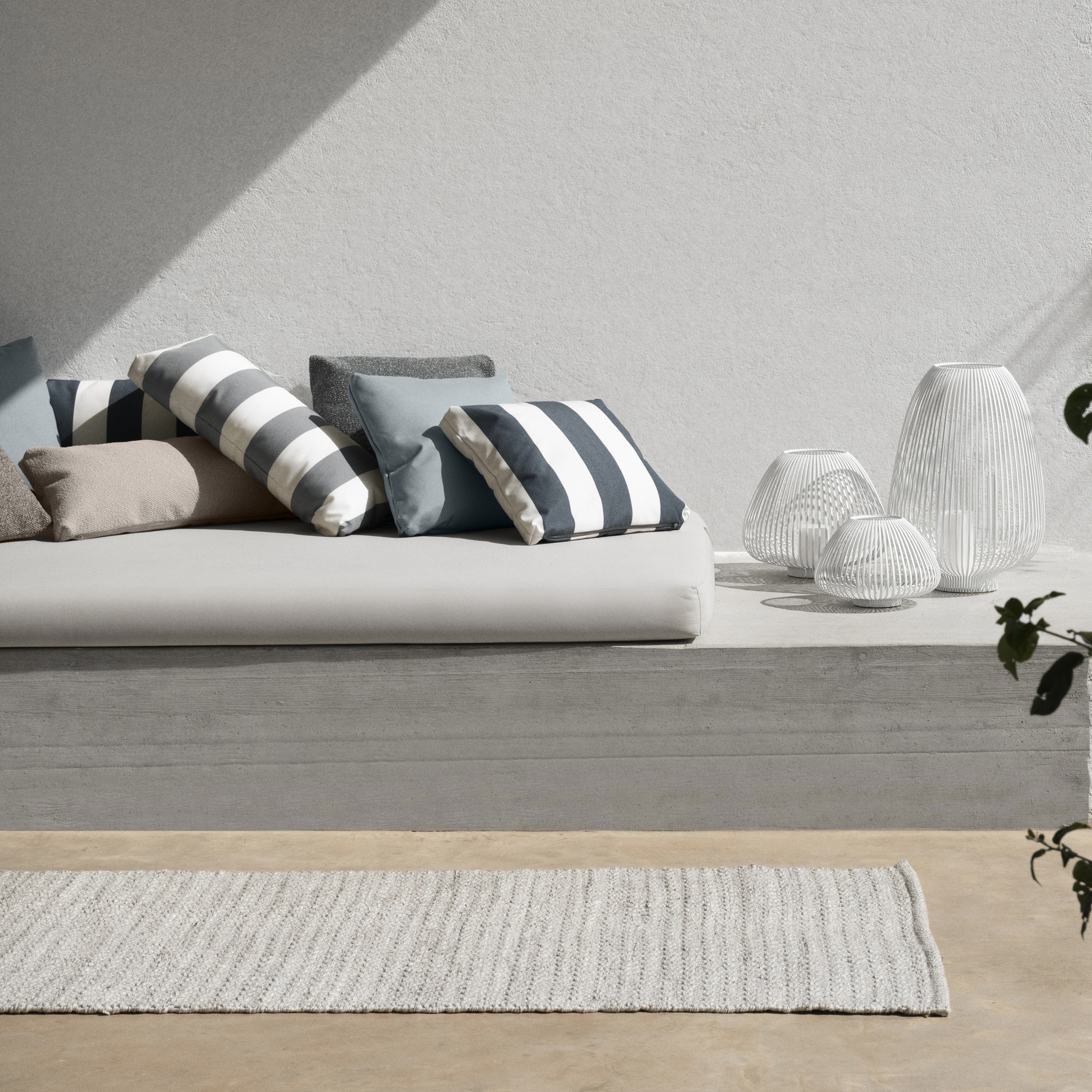 Modern living room with a gray sofa and striped cushions, light gray walls, and a wooden floor.