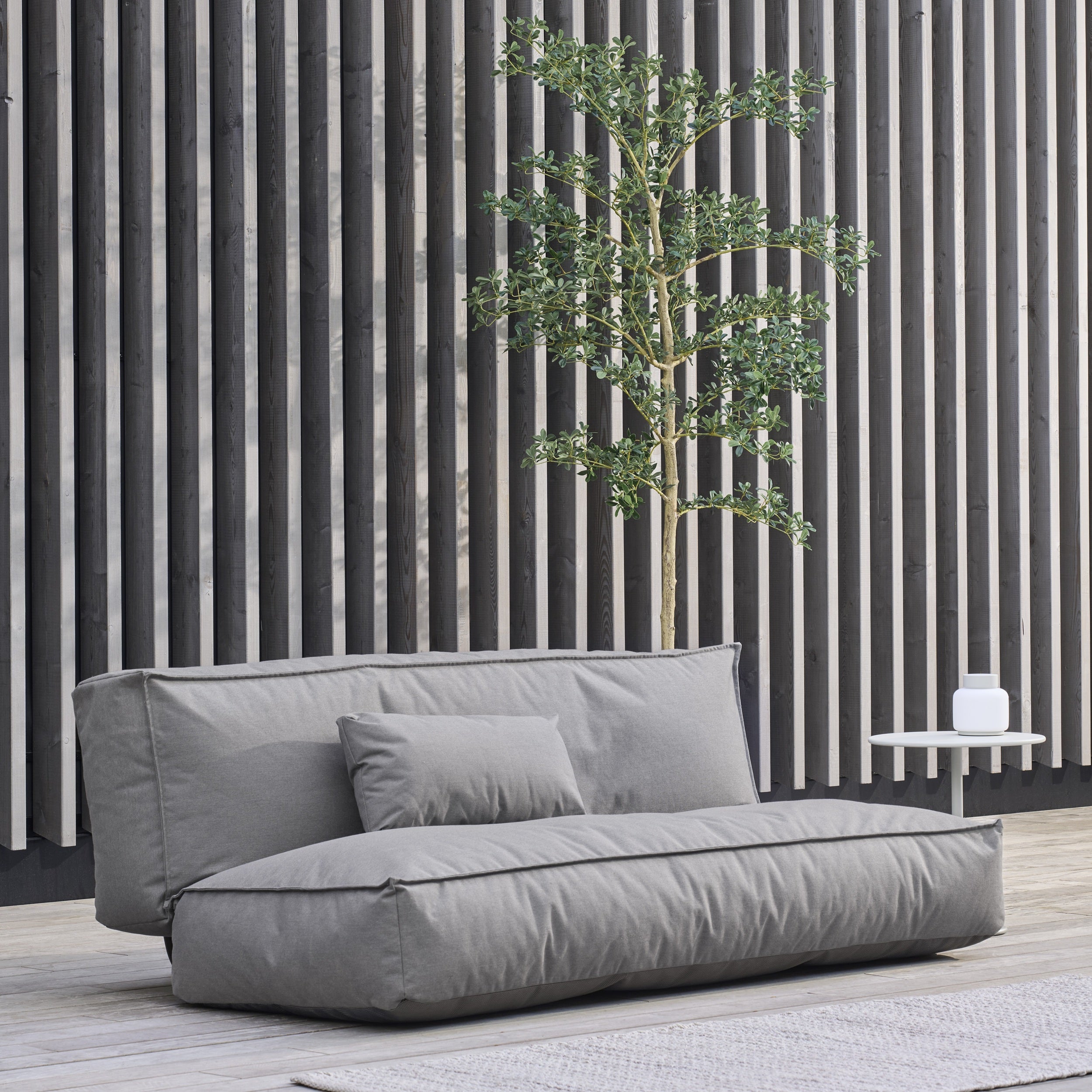 Gray outdoor sofa with a plant against a striped wall.