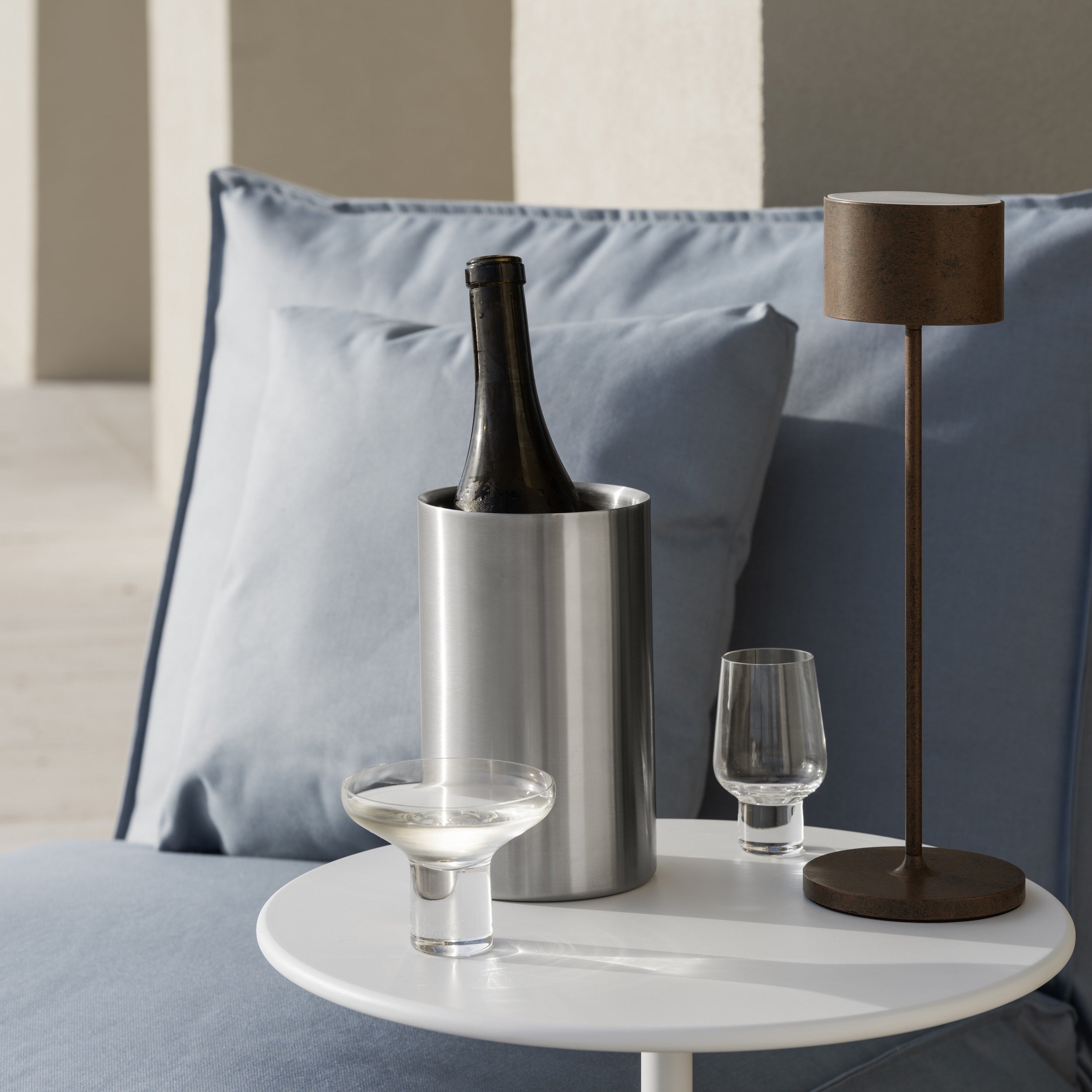 cozy outdoor lounge area with blomus KOYOI handblown glassware arranged on a white side table with a bottle of wine