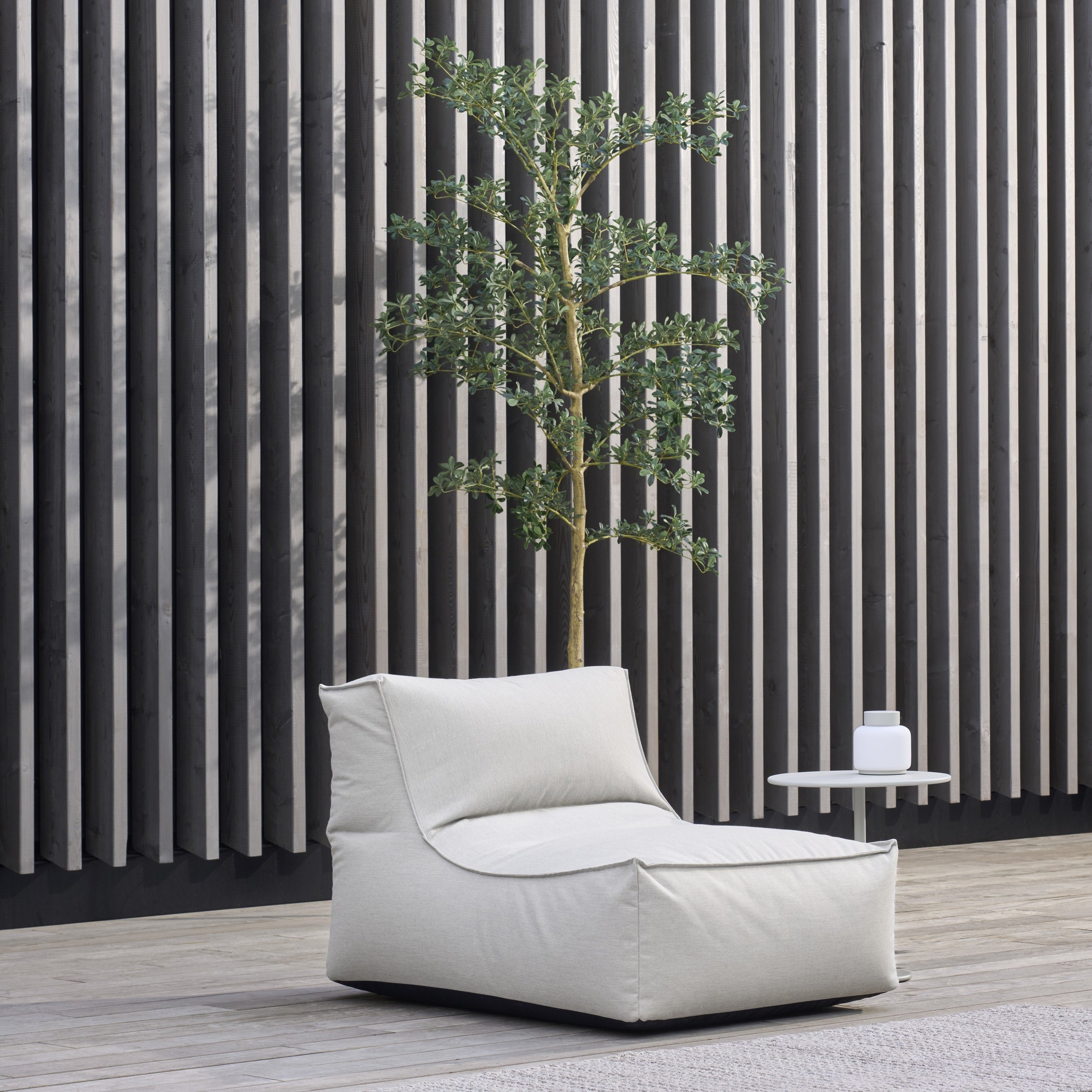 Modern outdoor chair with a plant and small table against a striped wall.