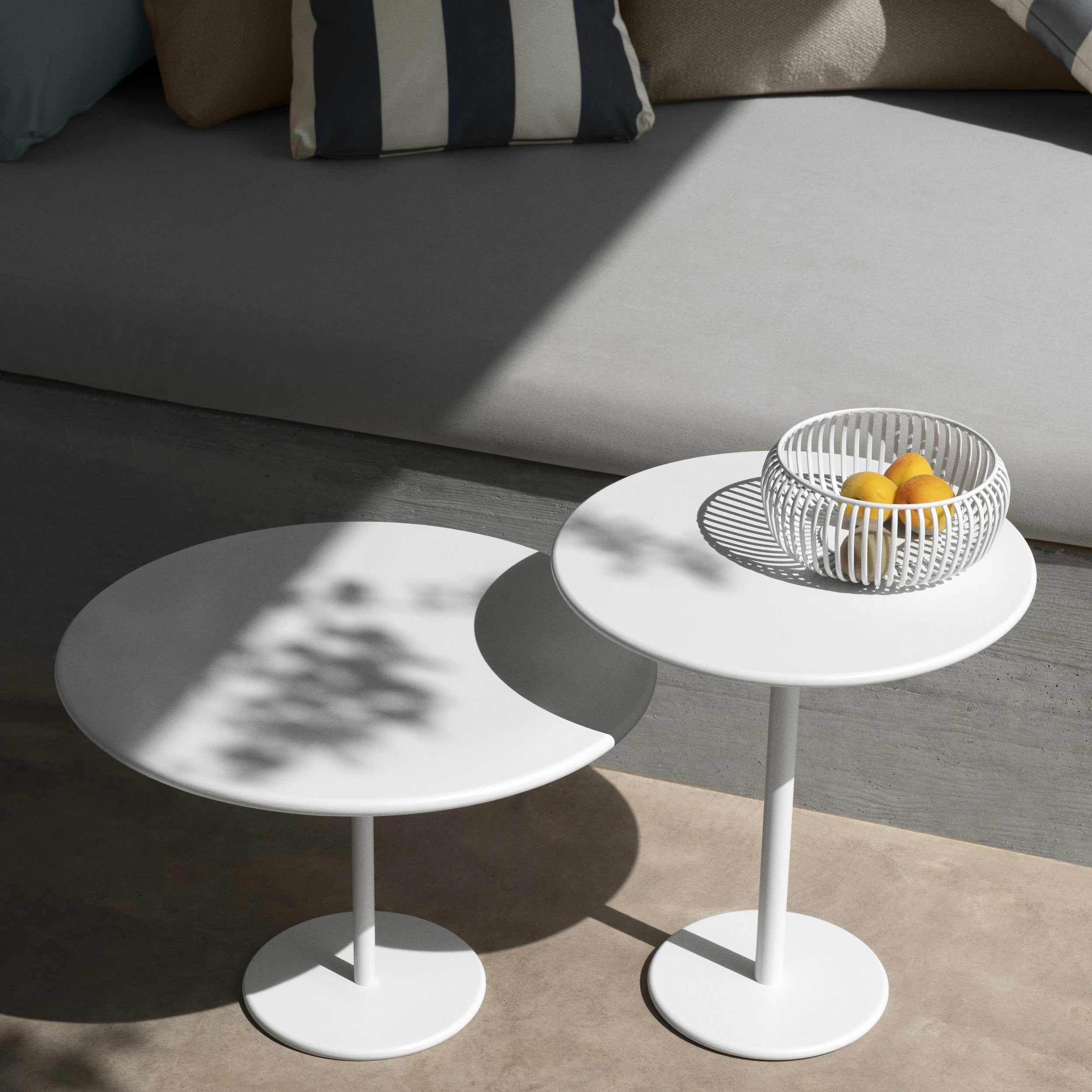 Two white STAY side tables with a basket of fruit on a neutral-colored floor.