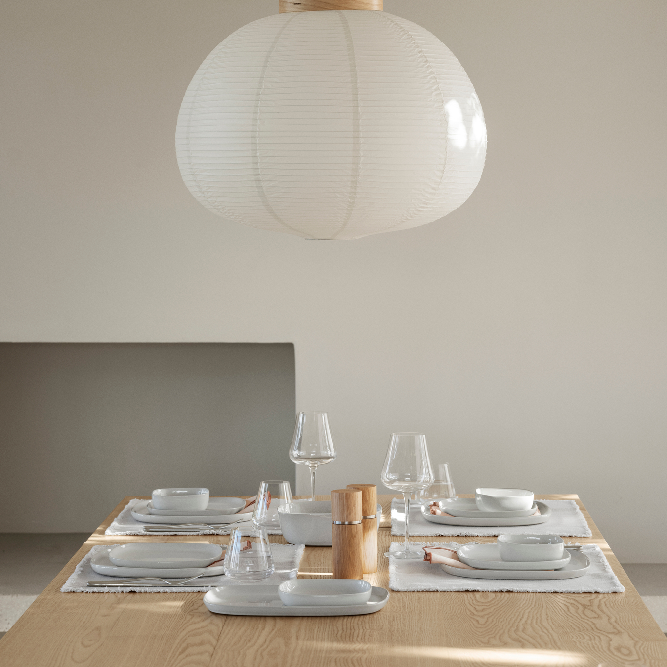 A wood table set with blomus moonbeam colored VAHLO Dishes including plates, bowls and serving dishes and blomus BELO Stemware in a neutral colored room.