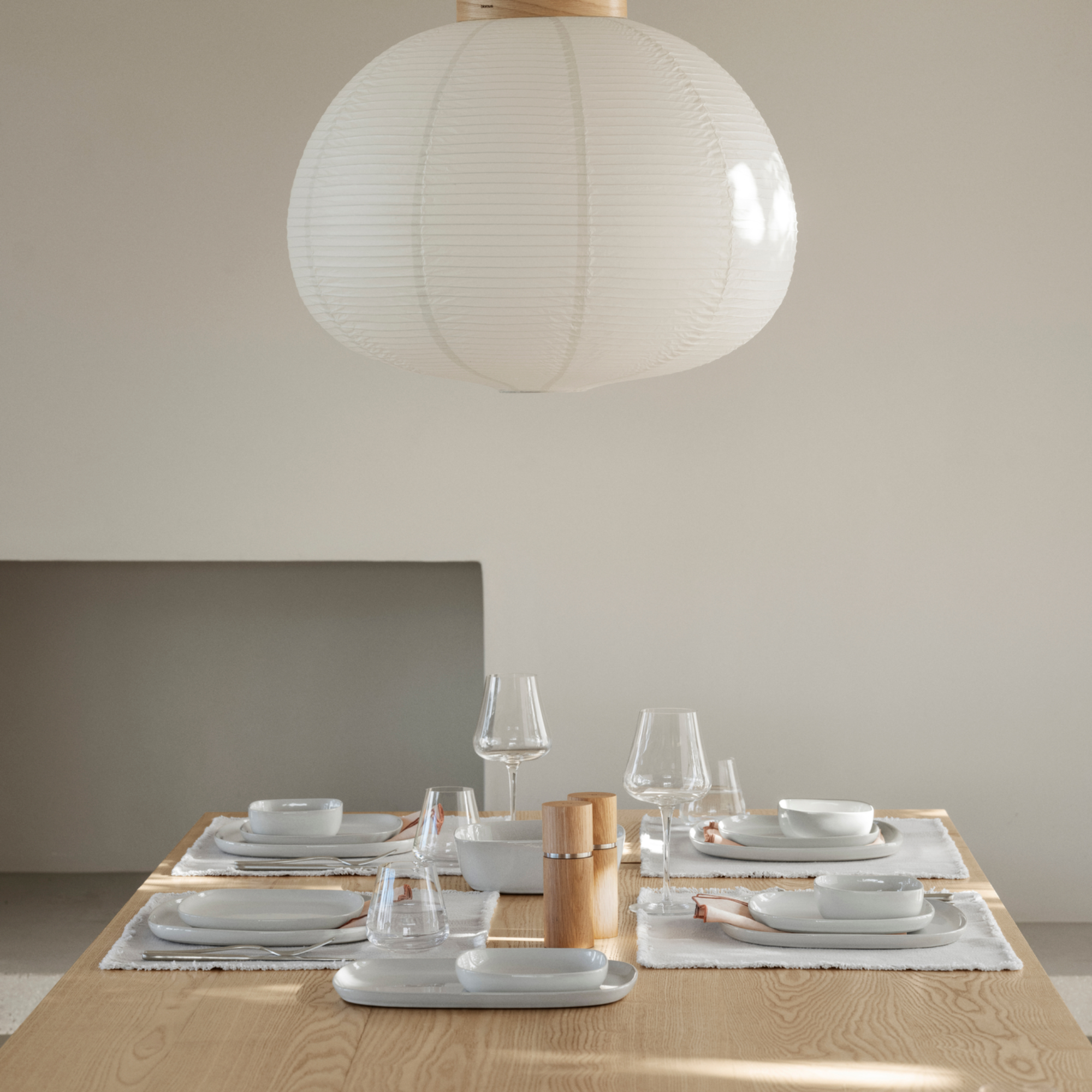 A wood table set with blomus moonbeam colored VAHLO Dishes including plates, bowls and serving dishes and blomus BELO Stemware in a neutral colored room.