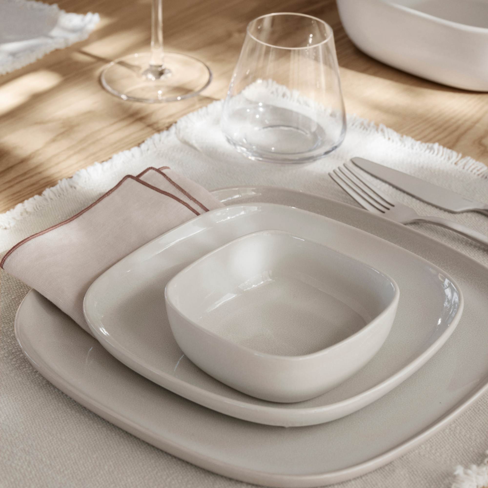 VAHLO Place Setting in Moonbeam on a place mat on a wood table. BELO Stemware shown also on the table. 