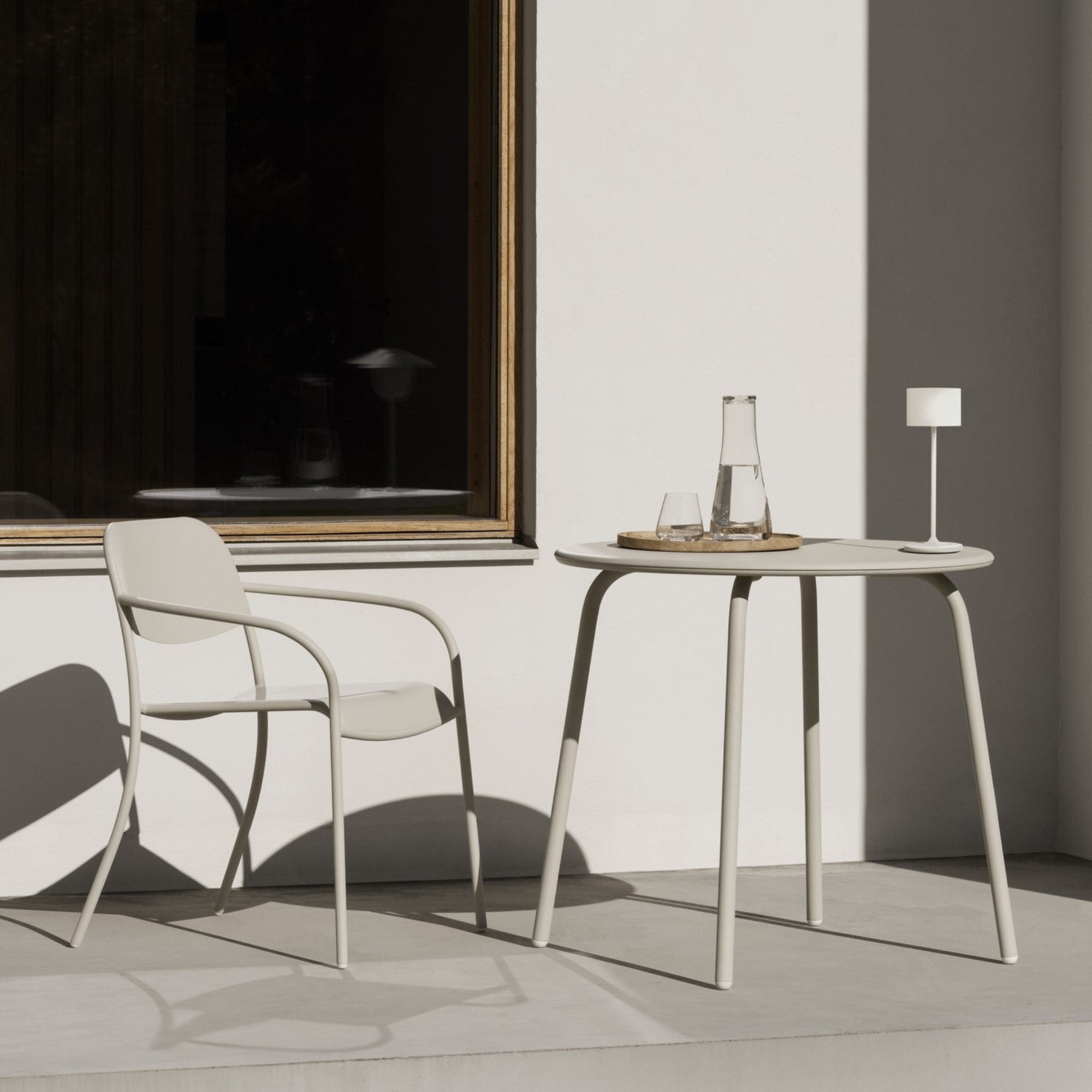 Round metal outdoor table with water glass and carafe with matching chair placed near by  