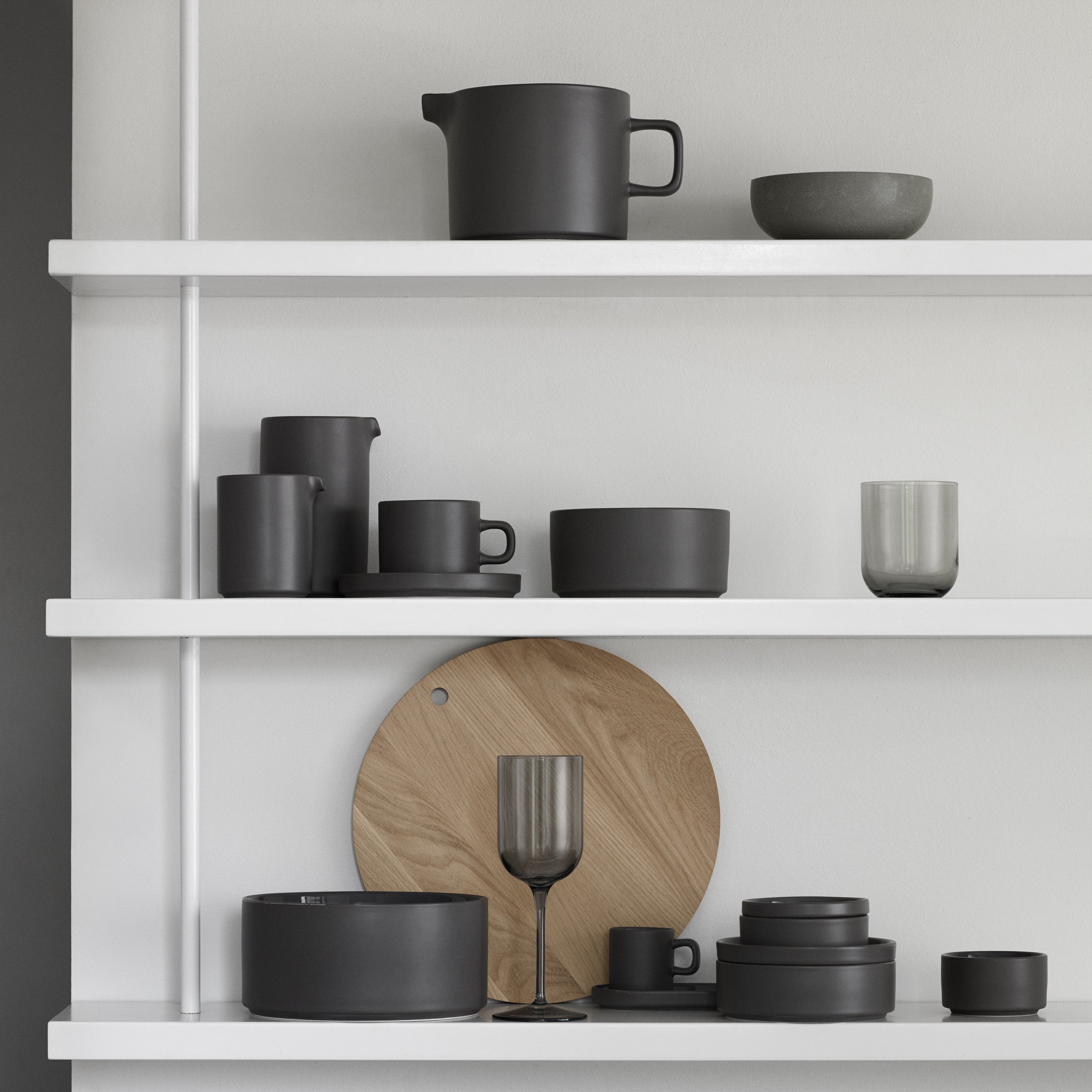 soft light reflecting on the matte exterior finish of stackable PILAR stoneware from blomus arranged upon minimalist white shelves