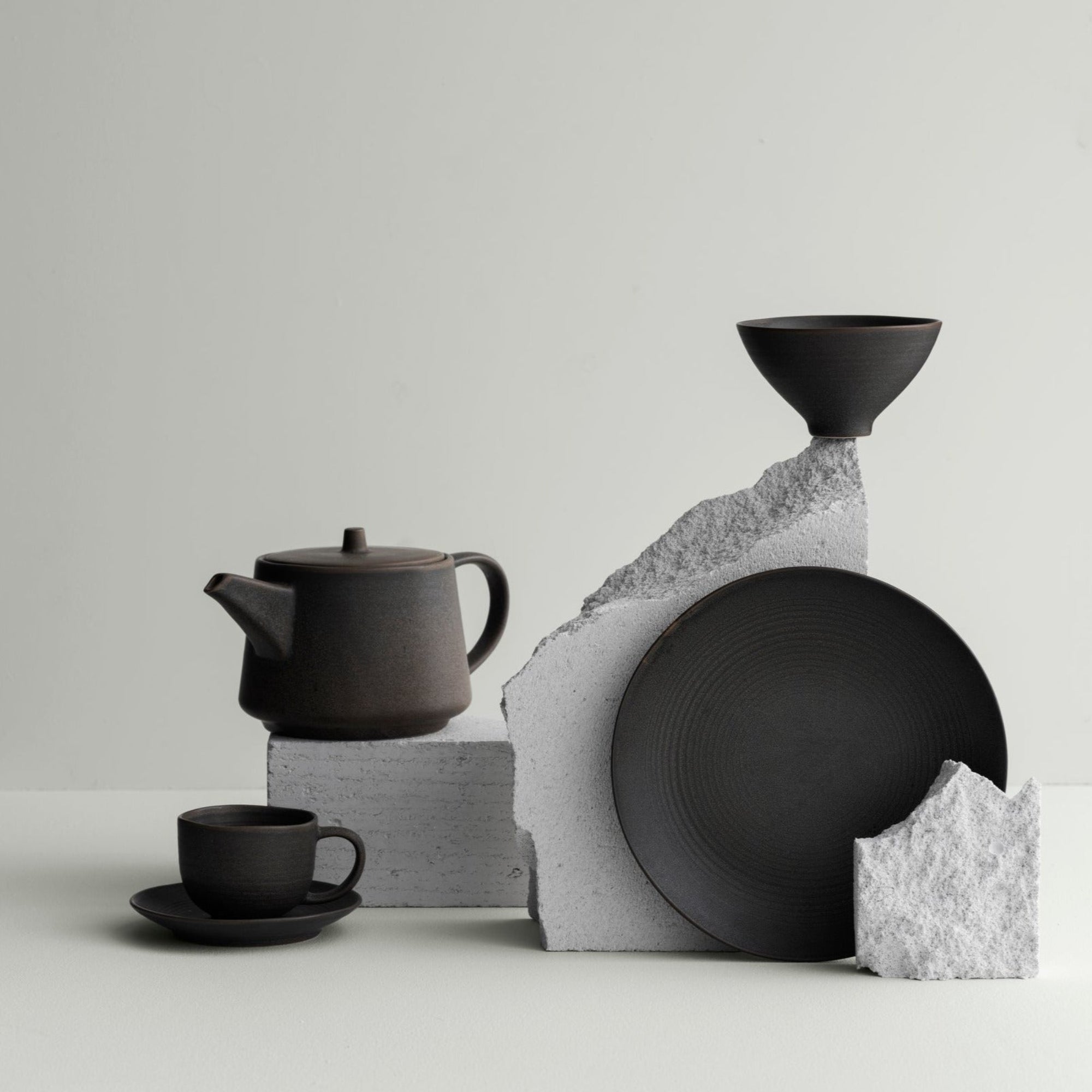 KUMI Ceramic tableware in Espresso brown placed on broken concrete in a minimalist setting