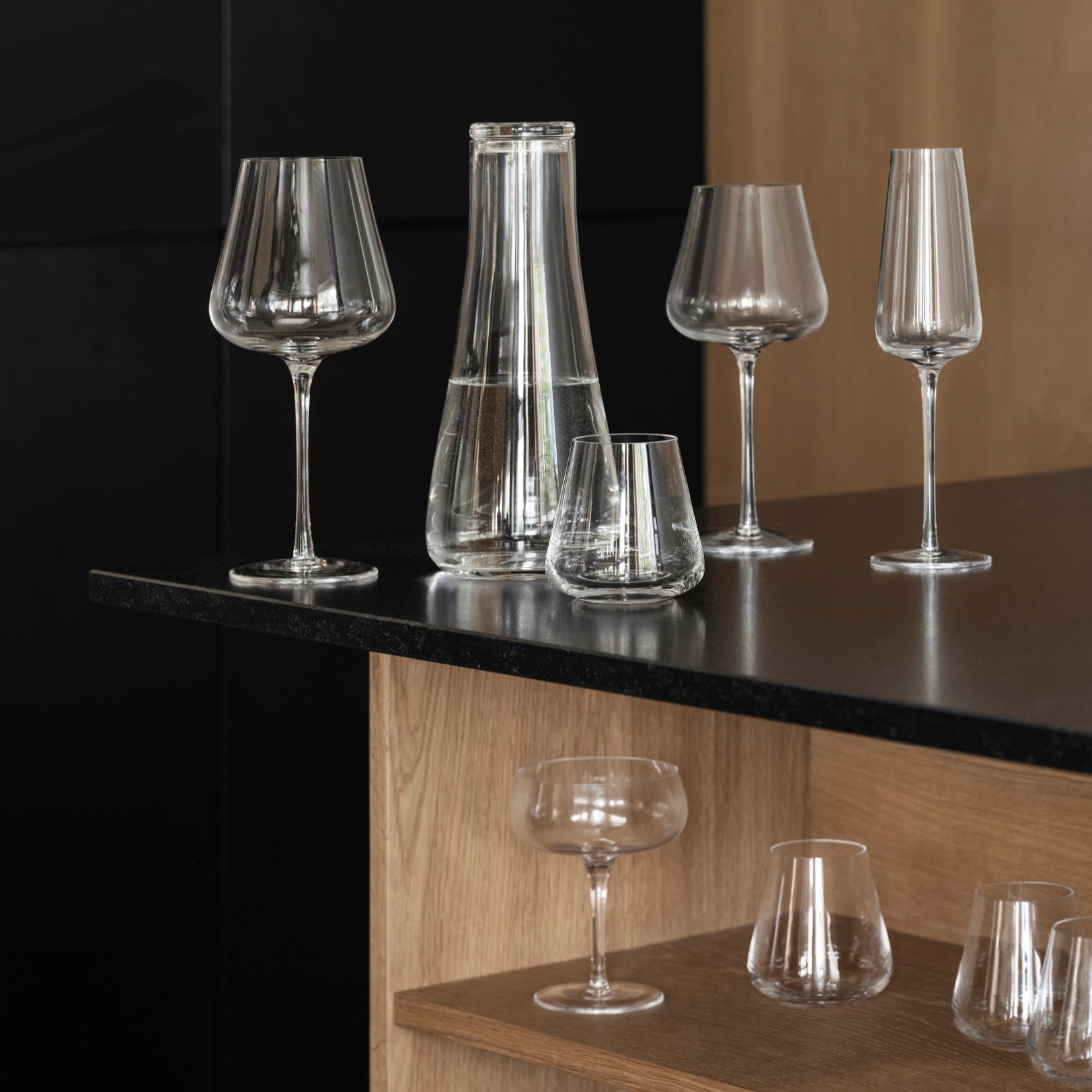 blomus BELO collection of unique handblown wine glasses on a black countertop with wooden shelves beneath
