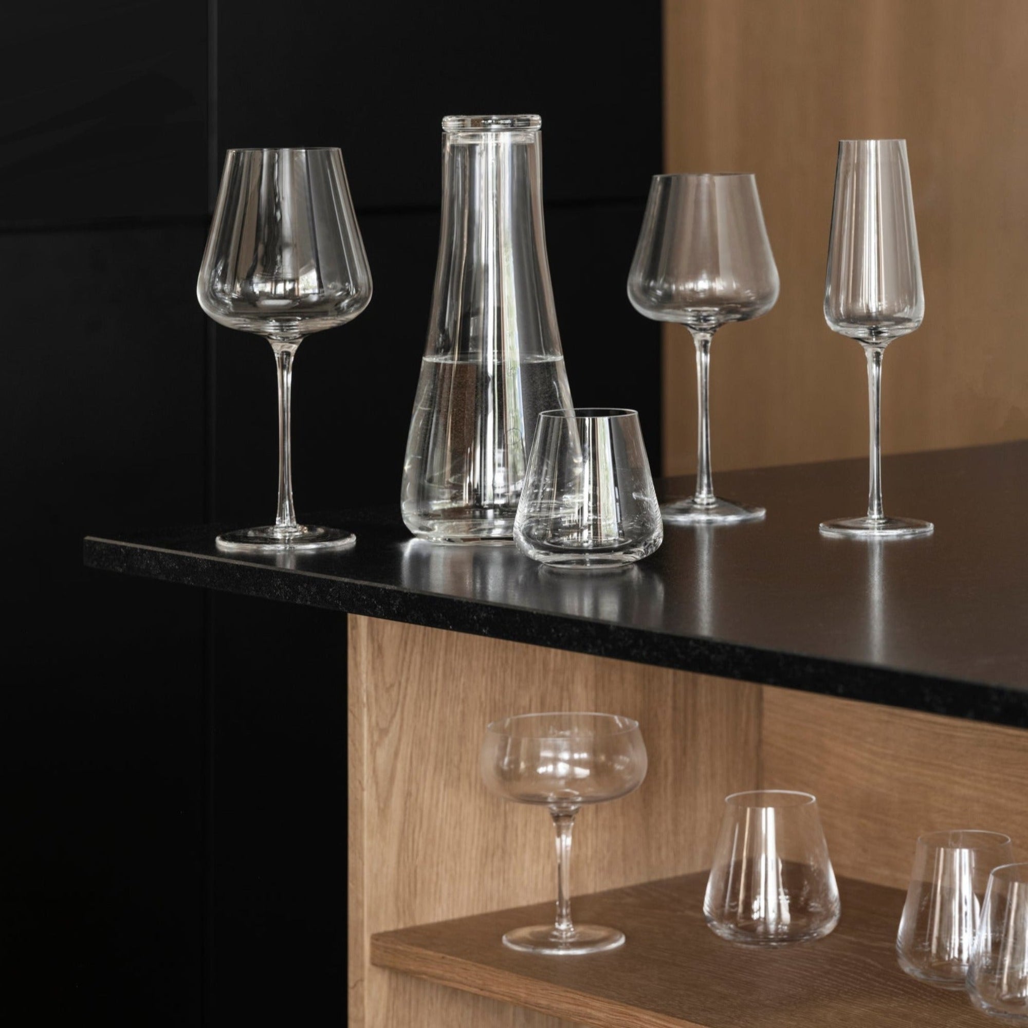 blomus BELO collection of unique handblown wine glasses on a black countertop with wooden shelves beneath