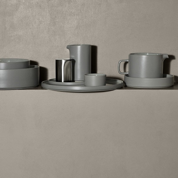 plates, bowls, and pitcher from the blomus PILAR collection of glazed ceramic dishware casually arranged upon a concrete ledge