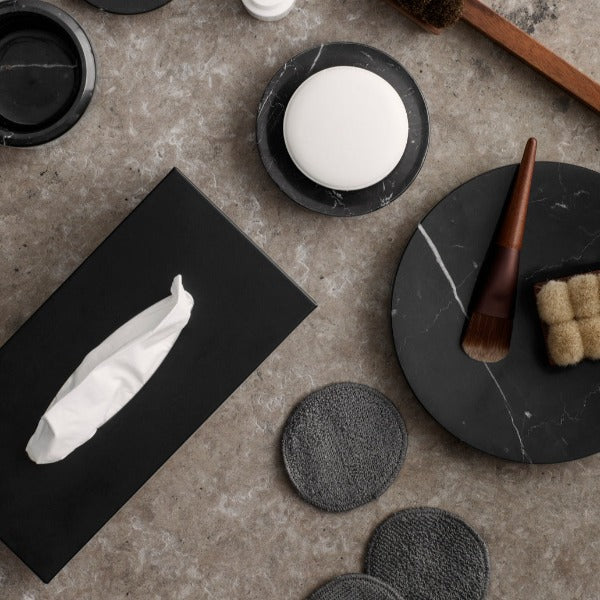 Marble bathroom counter with cosmetic supplies and black stainless steel tissue holder