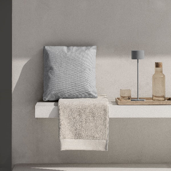 Concrete bench with pillow and wood tray holding glasses and an outdoor lamp