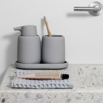 matte grey bathroom soap dispenser and tumbler set displayed on an exposed aggregate countertop