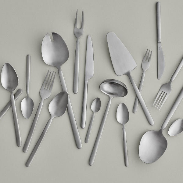 STELLA brushed stainless cutlery scattered across a minimalist grey background