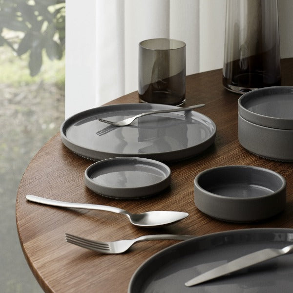 glazed ceramic PILAR dinnerware reflecting light from a large window arranged upon a modern walnut dining table with blomus cutlery and glassware